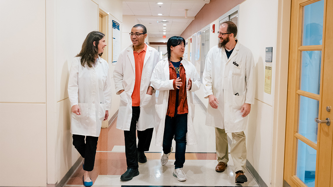 Two teachers and two students in labcoats walk down a hall in the Sullivan building.